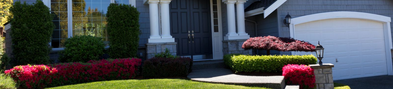 Front entrance of a house with a white garage door, manicured lawn, and colorful landscaping, symbolizing garage door maintenance tips from Garage Door Repair Aliso Viejo